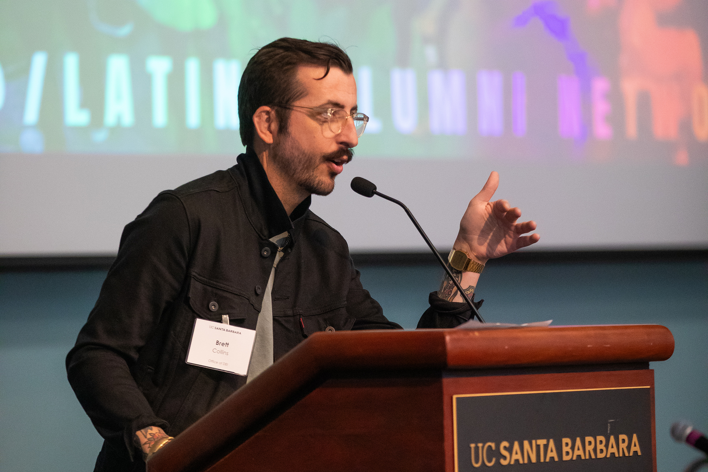 person with a mustache speaking at a podium